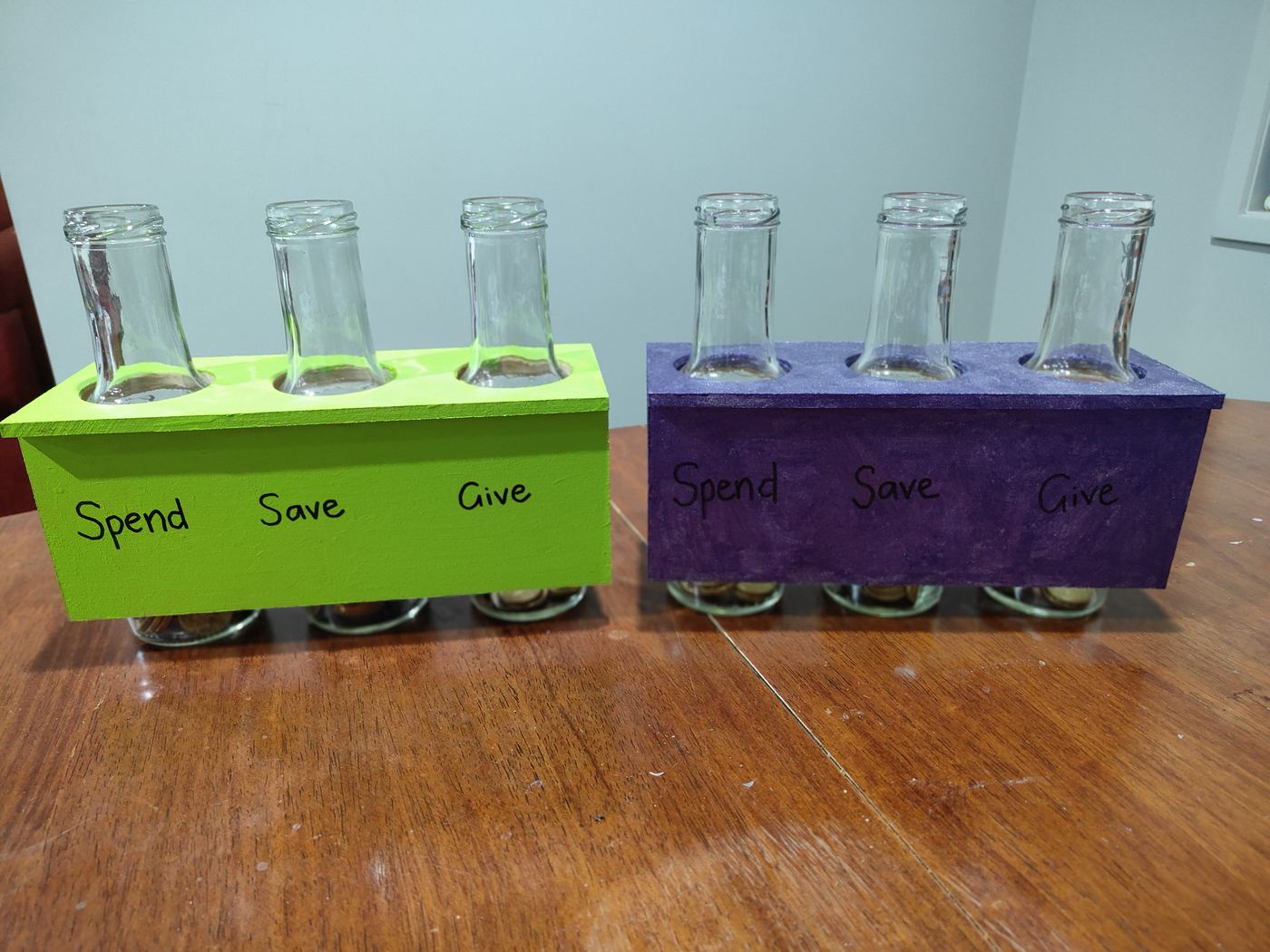 Two hand-painted wooden jar holders, green and purple, each labelled Spend, Save and Give, made by the kids