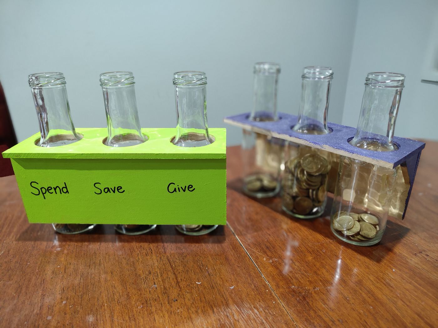 The same Spend, Save and Give jars viewed from the side, with $1 coins visible inside the Save and Give jars
